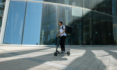 A man wearing a black bag riding a scooter on the road